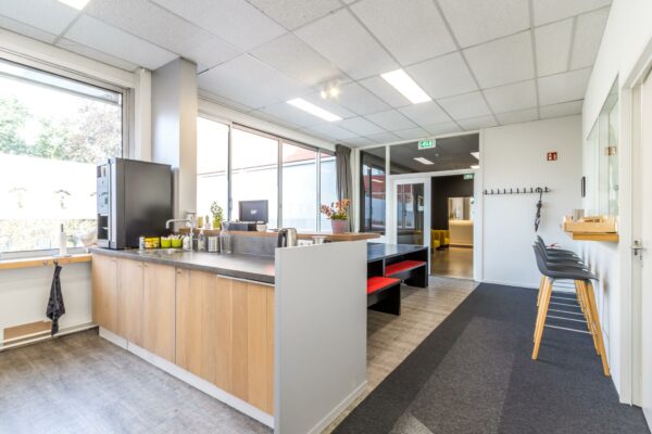 Moderne kantine met houten keuken, zitbanken met rode kussens en barkrukken in een kantoor aan de Jan van Eycklaan.